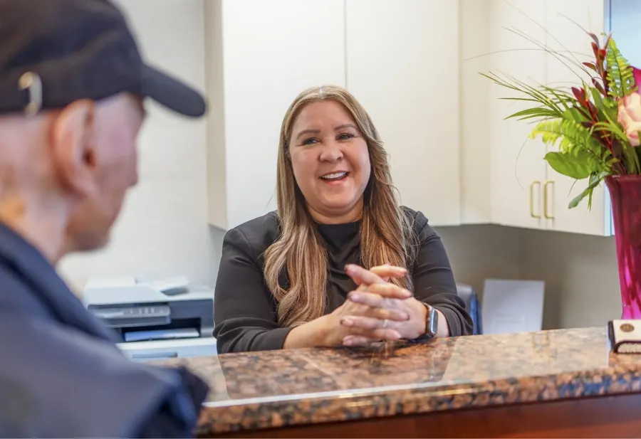 A team member smiling at the front desk as she talks with a patient.