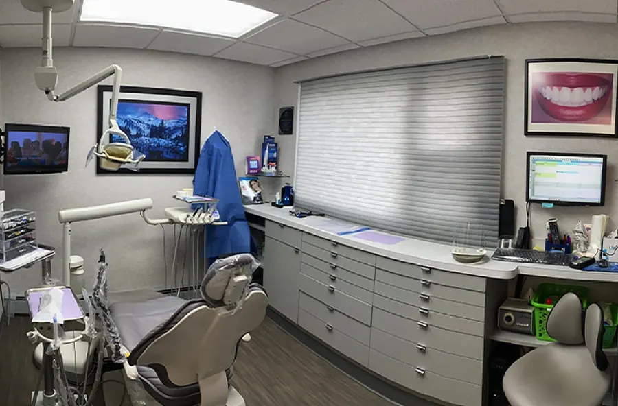 A treatment room with a grey chair, wide blinds and a smile photograph on the wall.