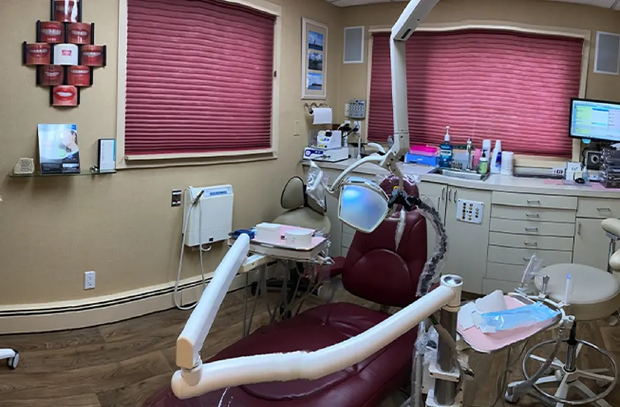A treatment room with a burgundy chair and rose-colored blinds.
