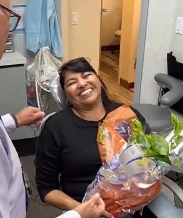 A patient holding flowers and smiling in the treatment chair on the day of her reveal.