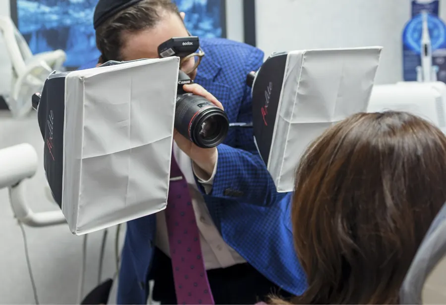 Dr. Ariel photographing a patient's smile with a camera and light panels in a treatment room.